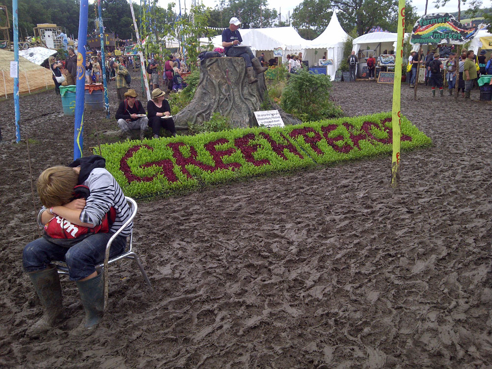How to survive hot and wet festivals - a guide to extreme festival weather - Glastonbury Festival boy with Greenpeace sign and mud